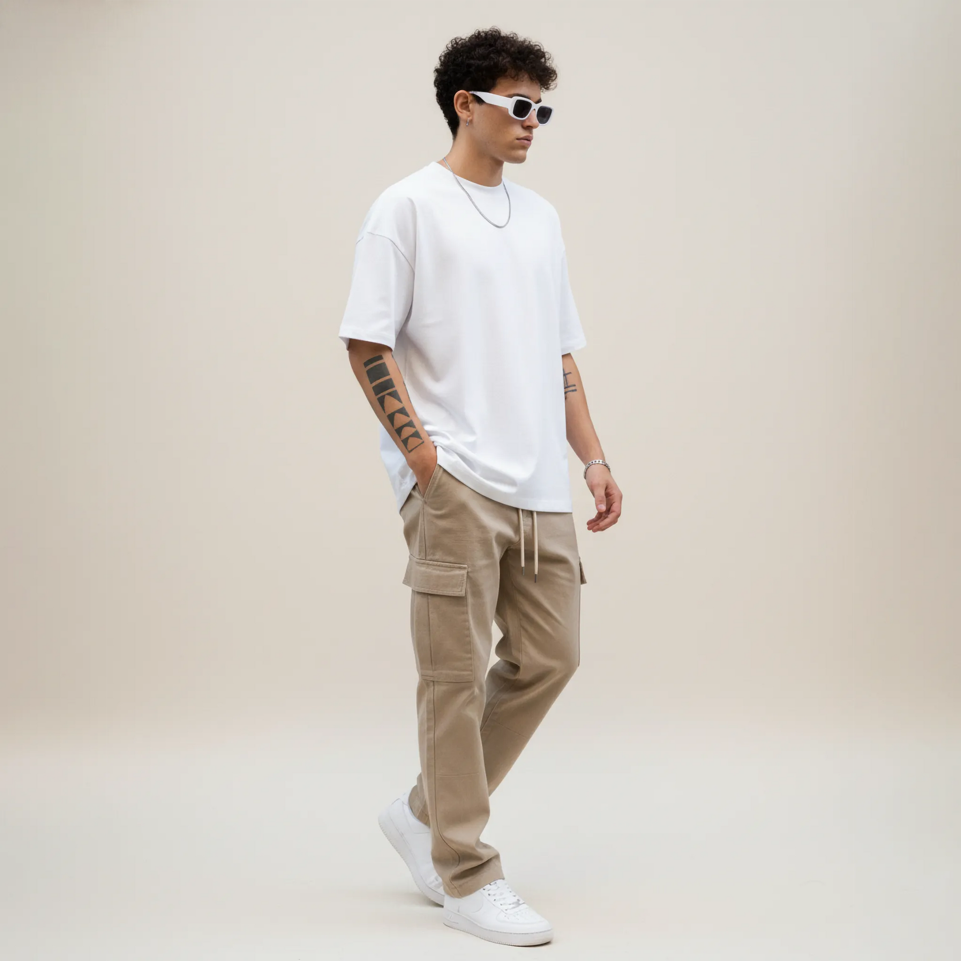 Man wearing a white t-shirt, beige cargo pants, and white sneakers on a plain background