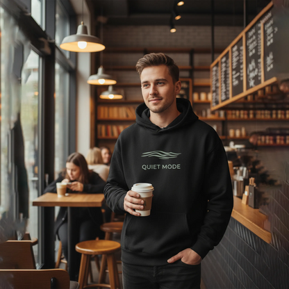 Man in a coffee shop wearing a black hoodie with 'Quiet Mode' text, holding a coffee cup.