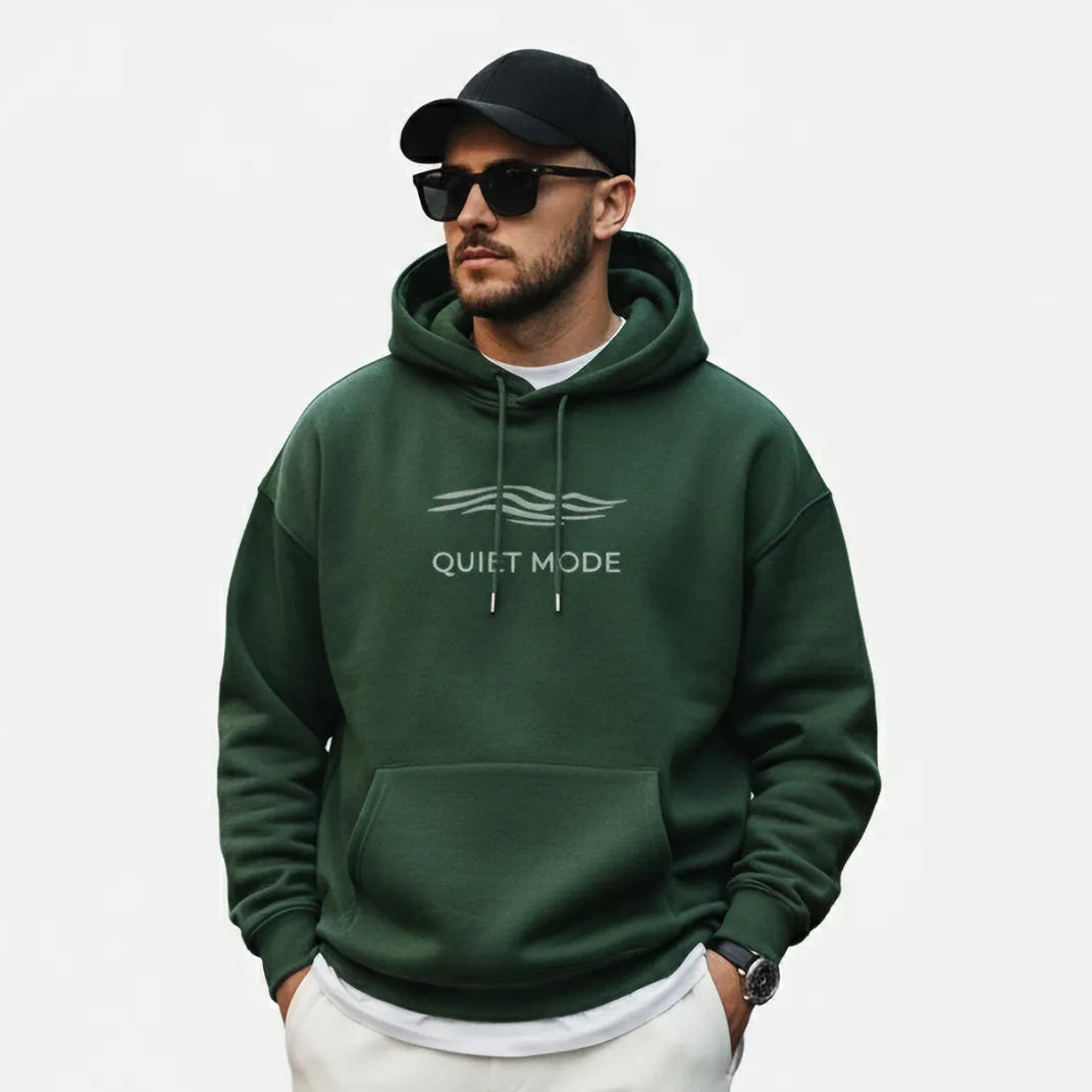 Man wearing a green hoodie with text, white pants, and gray sneakers on a white background