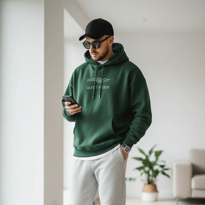 Man wearing a green hoodie and white pants standing in a modern living room.