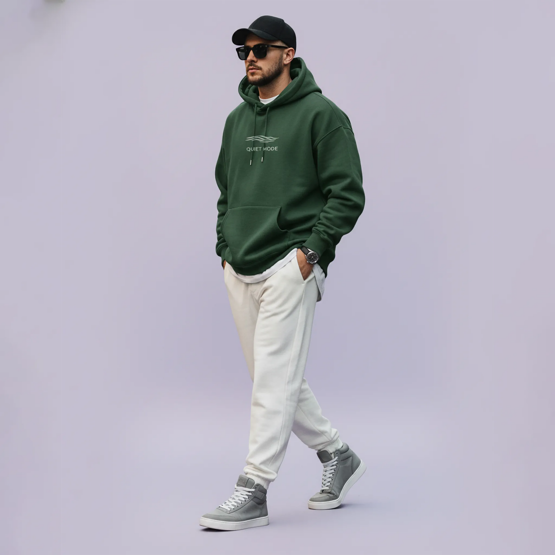 Man wearing a green hoodie, white pants, and gray sneakers on a light purple background